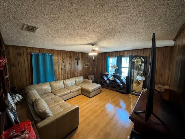 living room with wooden walls, ceiling fan, a textured ceiling, and hardwood / wood-style flooring