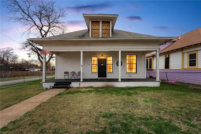 back house at dusk featuring covered porch and a lawn