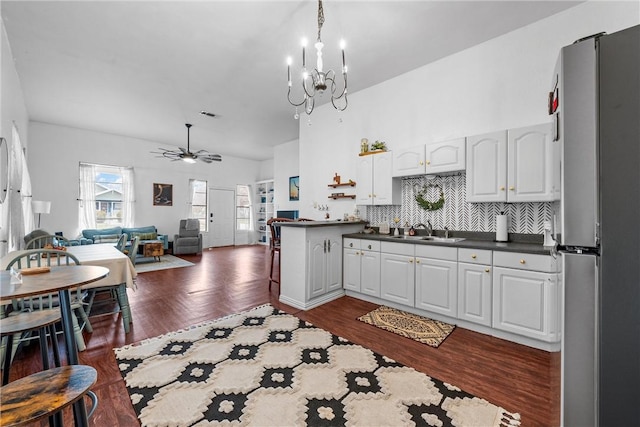 kitchen with tasteful backsplash, white cabinetry, stainless steel refrigerator, sink, and ceiling fan with notable chandelier