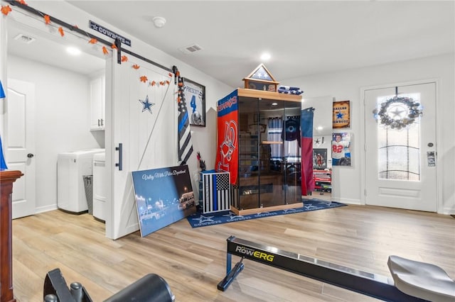 exercise area featuring a barn door, light hardwood / wood-style flooring, and washer and dryer