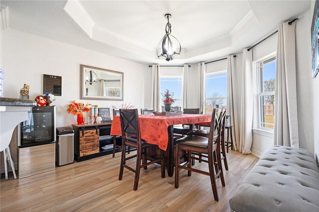 dining area featuring a raised ceiling, light hardwood / wood-style flooring, a chandelier, and ornamental molding