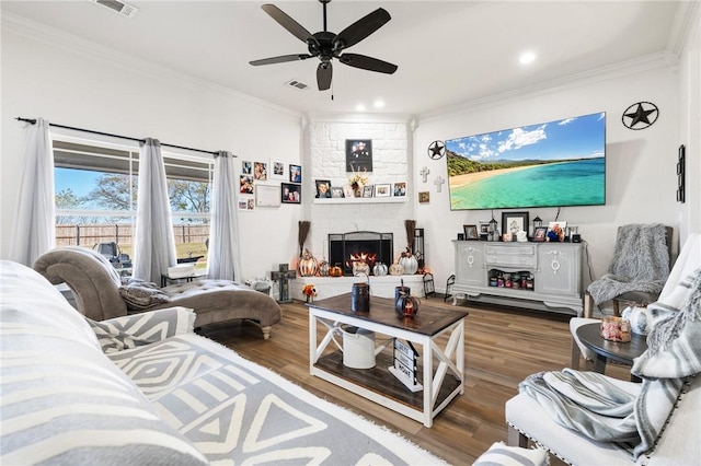 living room with dark hardwood / wood-style flooring, a stone fireplace, ceiling fan, and crown molding