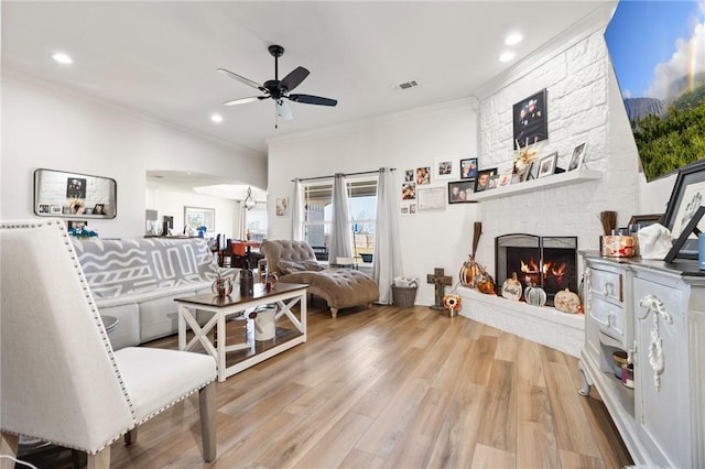 living room with light hardwood / wood-style floors, a stone fireplace, ceiling fan, and crown molding