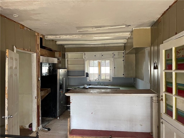 kitchen with kitchen peninsula, sink, black fridge with ice dispenser, and light wood-type flooring