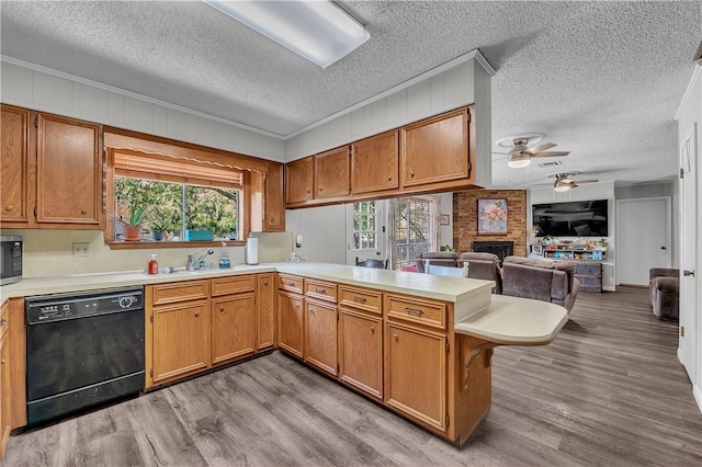 kitchen with sink, black dishwasher, light hardwood / wood-style flooring, kitchen peninsula, and a fireplace