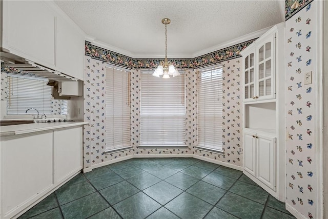 unfurnished dining area with an inviting chandelier, dark tile patterned flooring, crown molding, and a textured ceiling