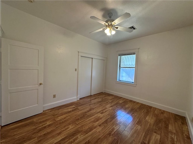 unfurnished bedroom with ceiling fan, wood-type flooring, a textured ceiling, and a closet