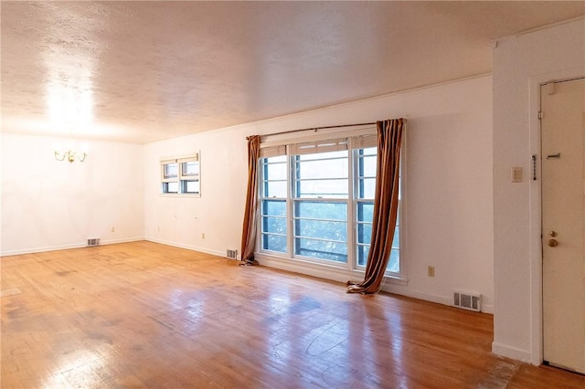 unfurnished room featuring a chandelier, light hardwood / wood-style flooring, and a textured ceiling