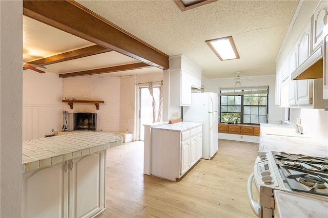 kitchen featuring ceiling fan, white cabinetry, gas range, tile countertops, and white fridge