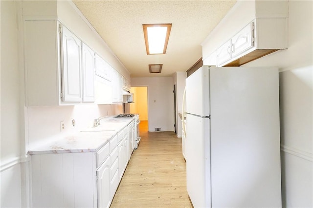 kitchen featuring sink, white appliances, white cabinetry, light hardwood / wood-style floors, and a textured ceiling