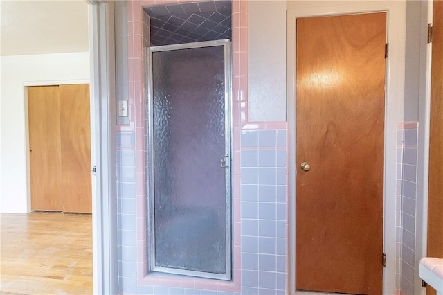 bathroom featuring wood-type flooring, a shower with shower door, and tile walls