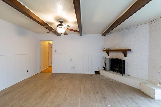 unfurnished living room featuring beamed ceiling, ceiling fan, a brick fireplace, and light hardwood / wood-style flooring