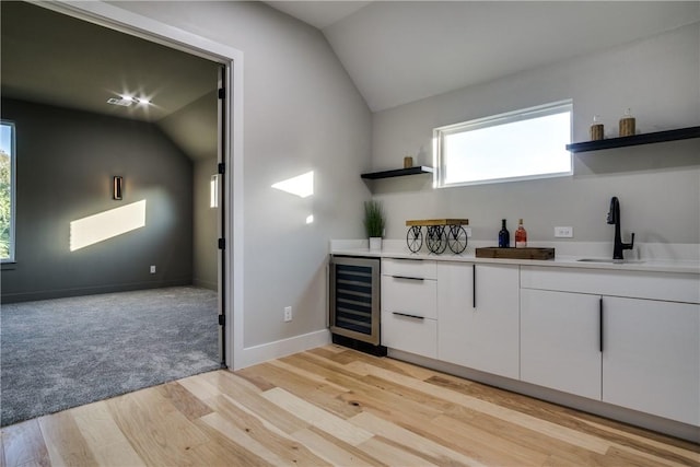 bar with lofted ceiling, white cabinets, sink, light wood-type flooring, and beverage cooler