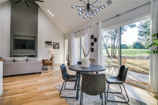 dining space featuring light wood-type flooring, high vaulted ceiling, and a chandelier