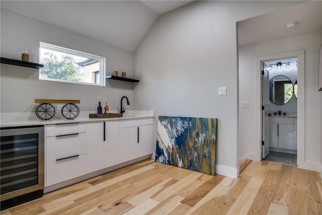 bar featuring sink, vaulted ceiling, light hardwood / wood-style flooring, white cabinetry, and beverage cooler