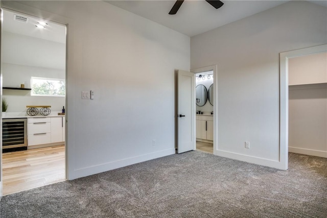 unfurnished bedroom with light carpet, ceiling fan, a spacious closet, beverage cooler, and a closet