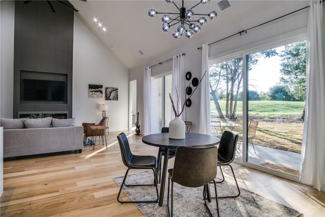 dining area with a notable chandelier, high vaulted ceiling, and light hardwood / wood-style flooring