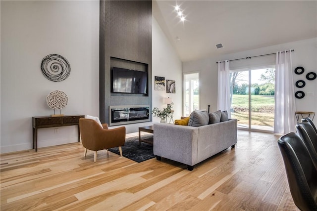 living room featuring a fireplace, light hardwood / wood-style floors, and high vaulted ceiling