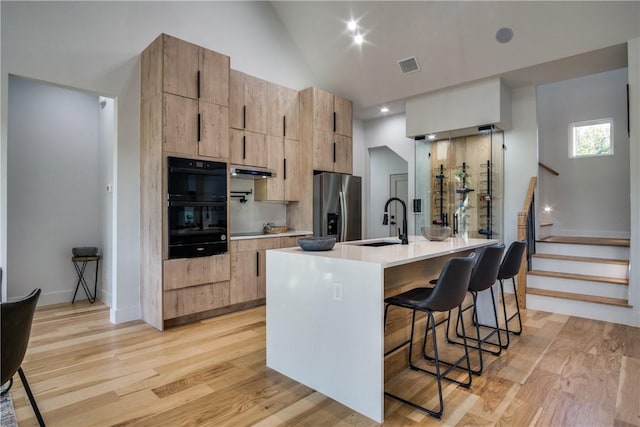 kitchen with a kitchen bar, a center island with sink, stainless steel refrigerator with ice dispenser, and light hardwood / wood-style flooring