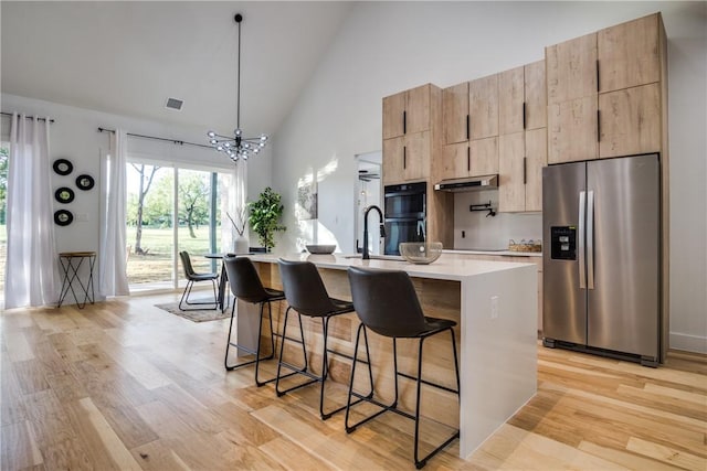 kitchen featuring stainless steel fridge with ice dispenser, high vaulted ceiling, an island with sink, a kitchen bar, and light wood-type flooring