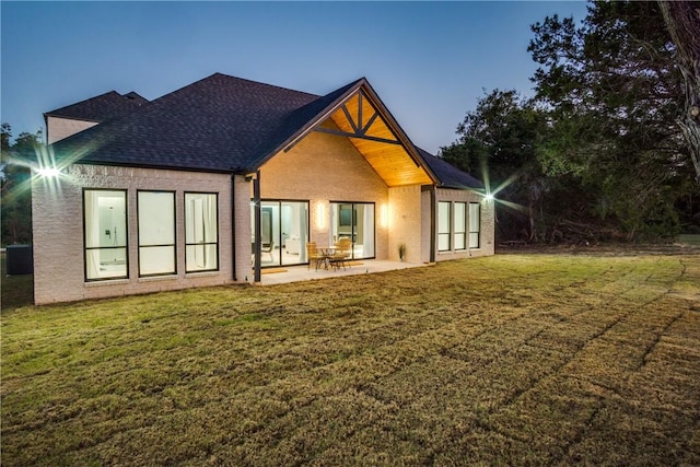 back house at dusk featuring a lawn and a patio