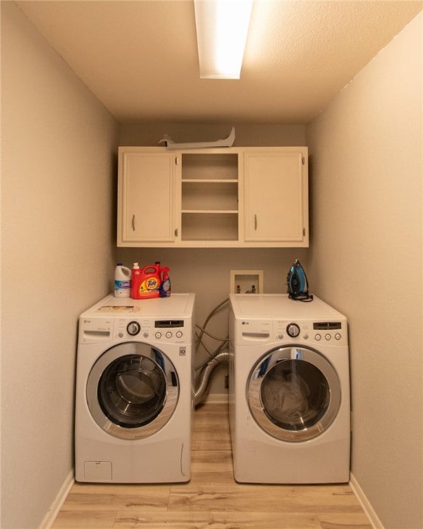 washroom with washing machine and clothes dryer, cabinets, and light wood-type flooring