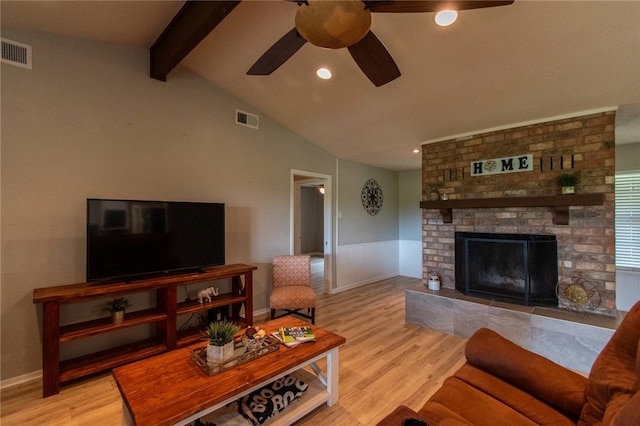 living room with vaulted ceiling with beams, light hardwood / wood-style floors, ceiling fan, and a brick fireplace