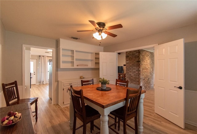 dining area with light hardwood / wood-style flooring, ceiling fan, and brick wall