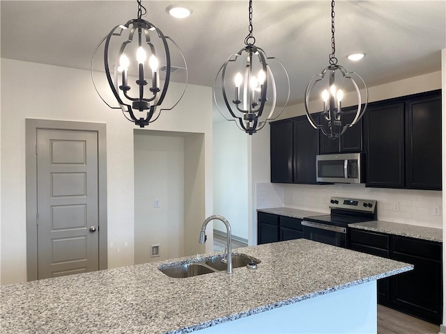 kitchen featuring appliances with stainless steel finishes, a chandelier, sink, and light stone countertops