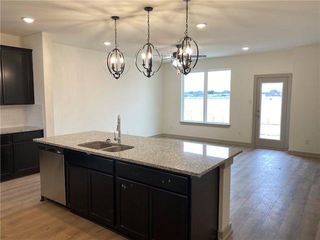 kitchen featuring dishwasher, sink, a kitchen island with sink, light stone counters, and light wood-type flooring