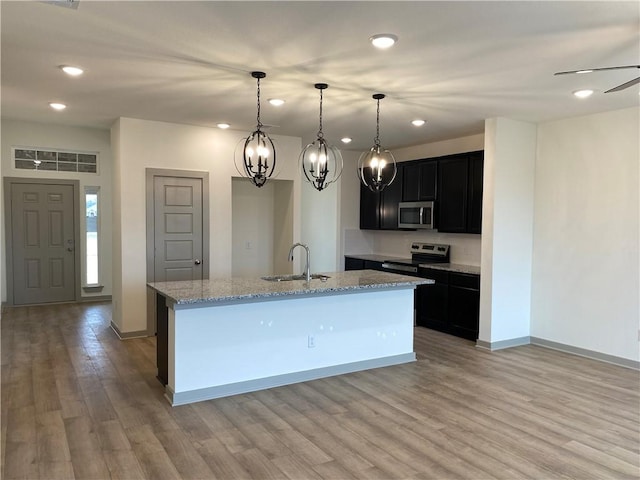 kitchen with pendant lighting, sink, light stone counters, stainless steel appliances, and a center island with sink