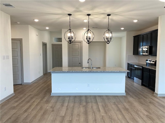 kitchen featuring pendant lighting, sink, stainless steel appliances, and an island with sink