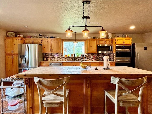 kitchen with tile countertops, stainless steel appliances, a breakfast bar, decorative backsplash, and decorative light fixtures