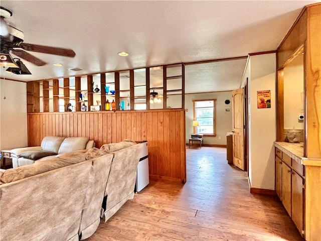 living room featuring a ceiling fan, baseboards, a textured ceiling, and light wood finished floors