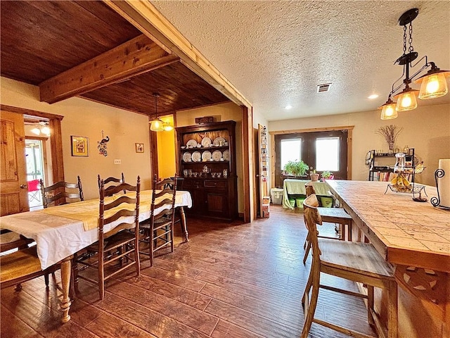 dining room featuring a textured ceiling, dark wood-type flooring, beamed ceiling, and visible vents