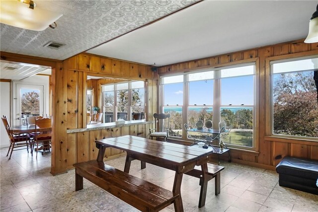 dining area with wooden walls, a water view, and a healthy amount of sunlight