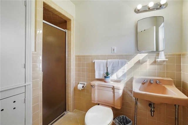 bathroom with tile patterned floors, toilet, tile walls, and a shower with shower door