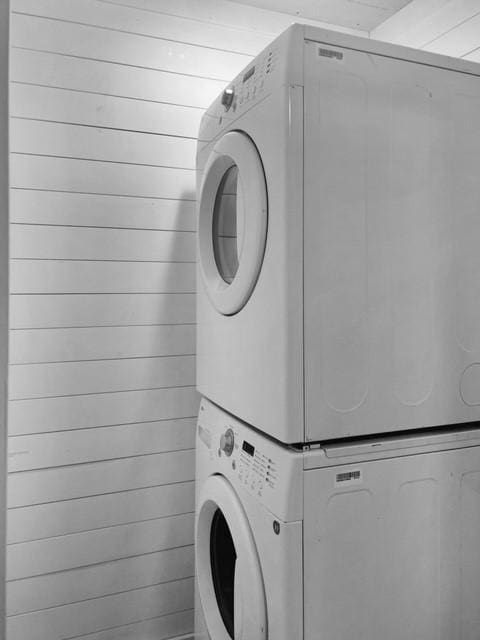 laundry area featuring stacked washing maching and dryer and wooden walls