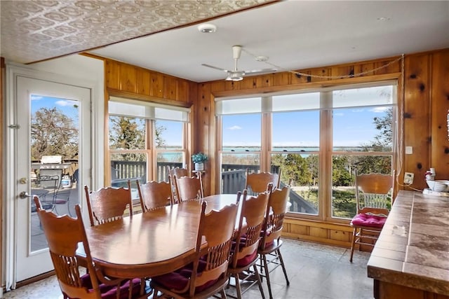 dining space with a wealth of natural light, a water view, wood walls, and ceiling fan