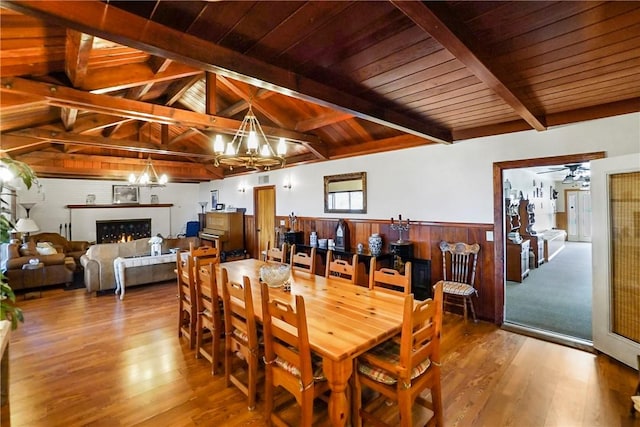 dining space featuring hardwood / wood-style floors, vaulted ceiling with beams, wood walls, and an inviting chandelier