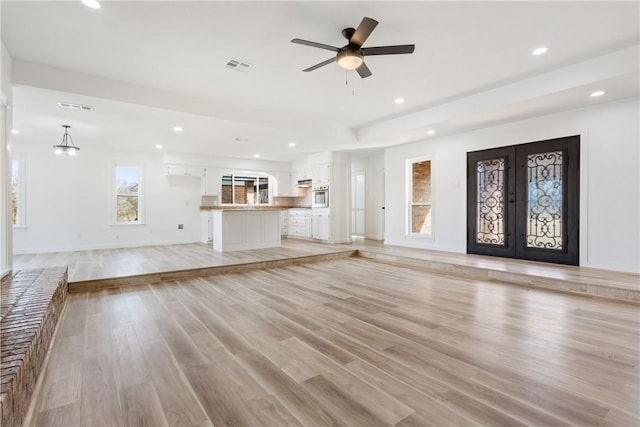 unfurnished living room featuring french doors, ceiling fan with notable chandelier, and light hardwood / wood-style flooring