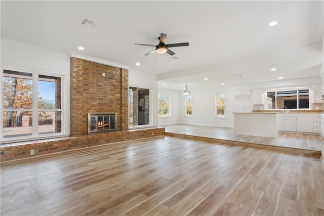 unfurnished living room featuring light wood-type flooring, a brick fireplace, and ceiling fan