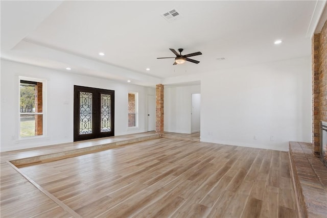 unfurnished living room with ceiling fan, french doors, light hardwood / wood-style floors, and a brick fireplace