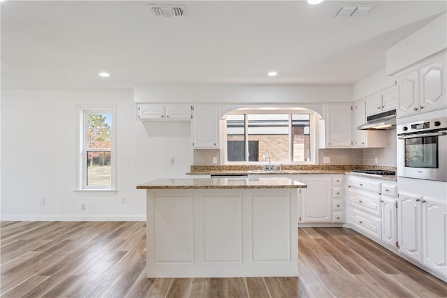 kitchen featuring light stone countertops, stainless steel appliances, white cabinets, light hardwood / wood-style floors, and a kitchen island