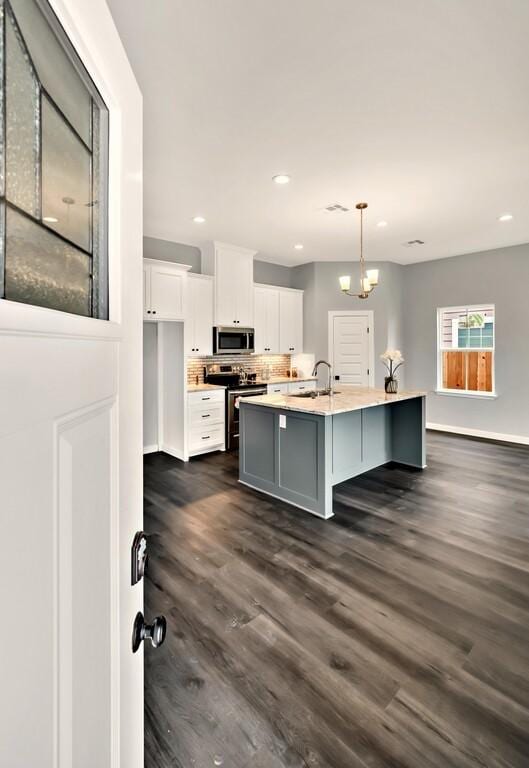 kitchen with a kitchen island with sink, dark hardwood / wood-style floors, appliances with stainless steel finishes, decorative light fixtures, and white cabinetry