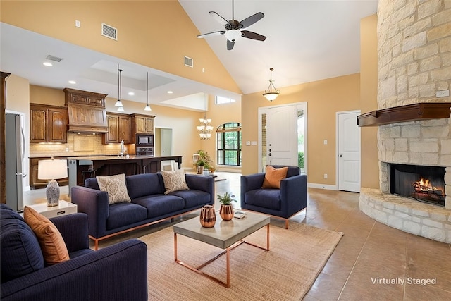 tiled living room with ceiling fan with notable chandelier, a high ceiling, and a stone fireplace