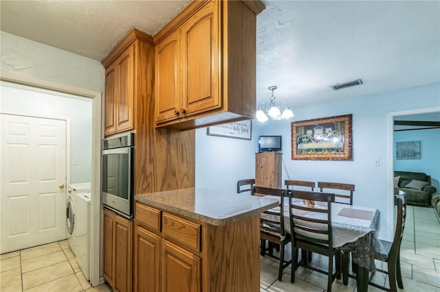 kitchen featuring stainless steel oven, light tile patterned floors, pendant lighting, a notable chandelier, and independent washer and dryer