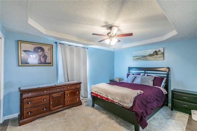 bedroom with ceiling fan, a textured ceiling, and a tray ceiling