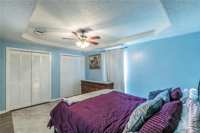 bedroom with ceiling fan, a raised ceiling, a textured ceiling, and multiple closets