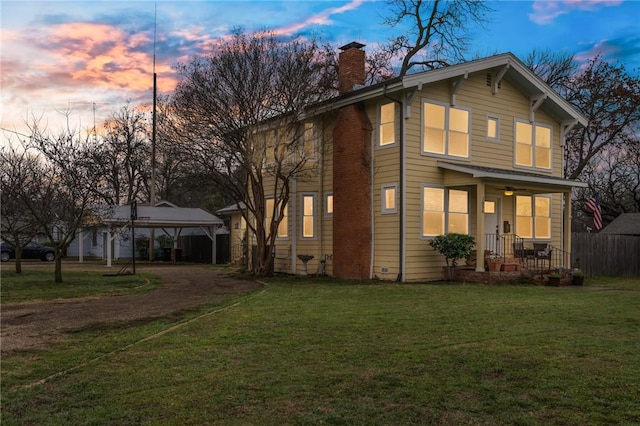 back house at dusk with a lawn and a carport